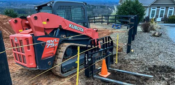 A red Kubota skid steer loader is operating on a construction site, surrounded by safety barriers and cones.