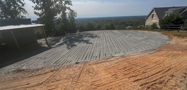 A gravel driveway leading to a barn, with tire tracks visible in the soil and a scenic view of trees and open land in the background.